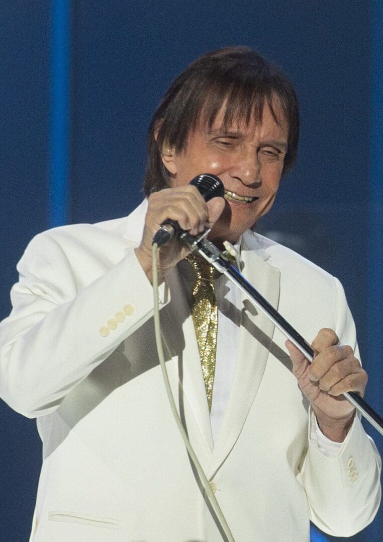 Singer in white suit holding microphone.