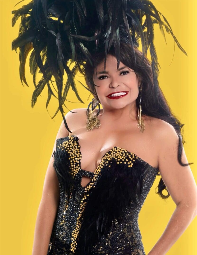 Woman in feathered costume, smiling, yellow background.