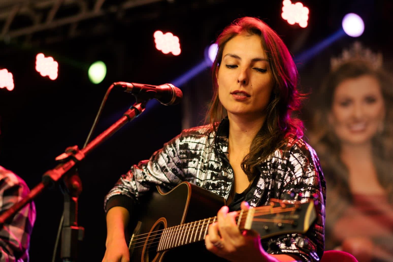 Woman playing guitar on stage, colorful lights.
