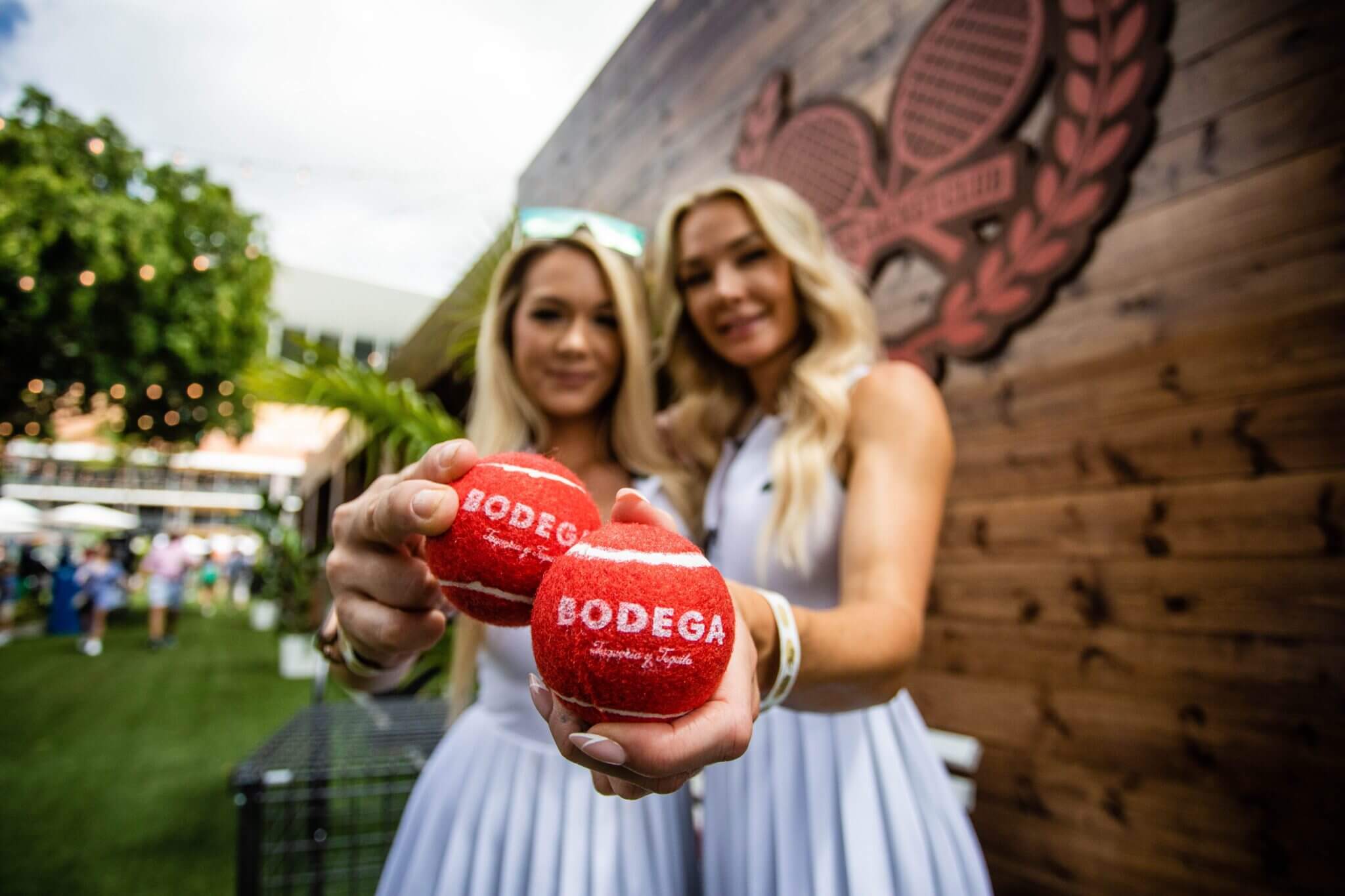 Two women holding red Bodega wine glasses and smiling outdoors.