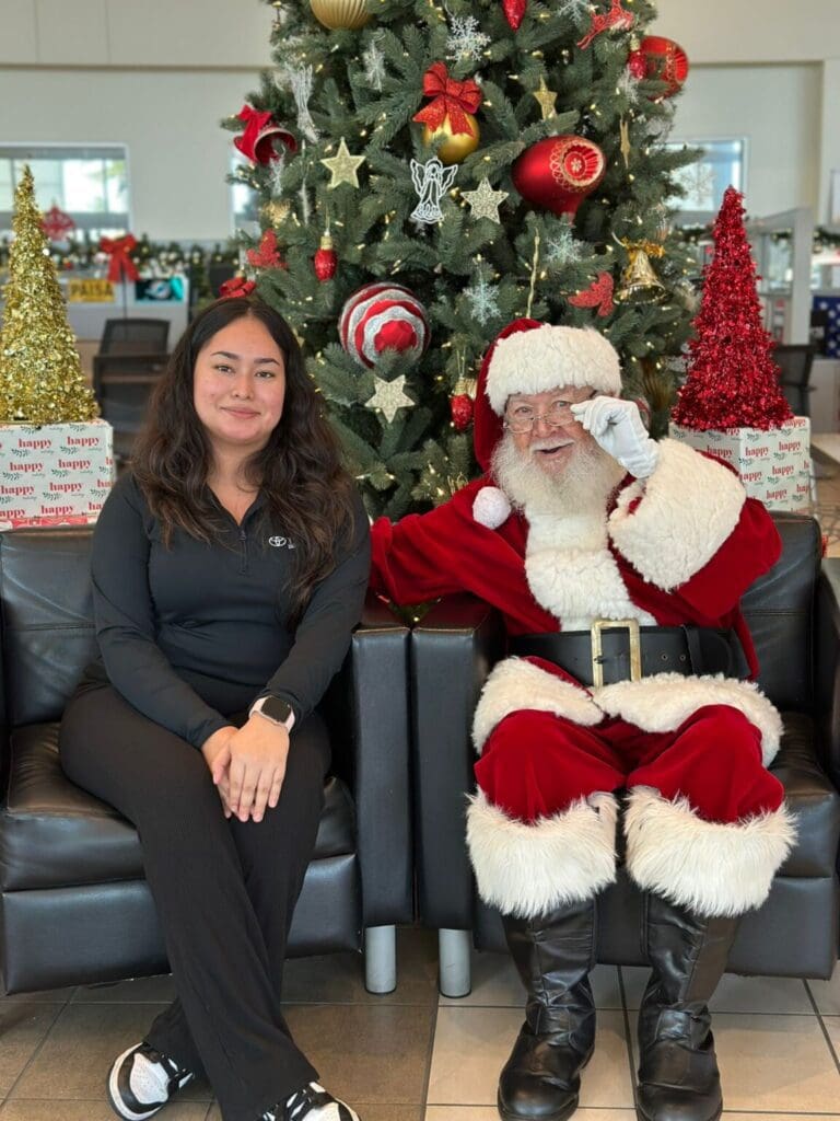 Woman sitting next to Santa Claus indoors with Christmas decorations.