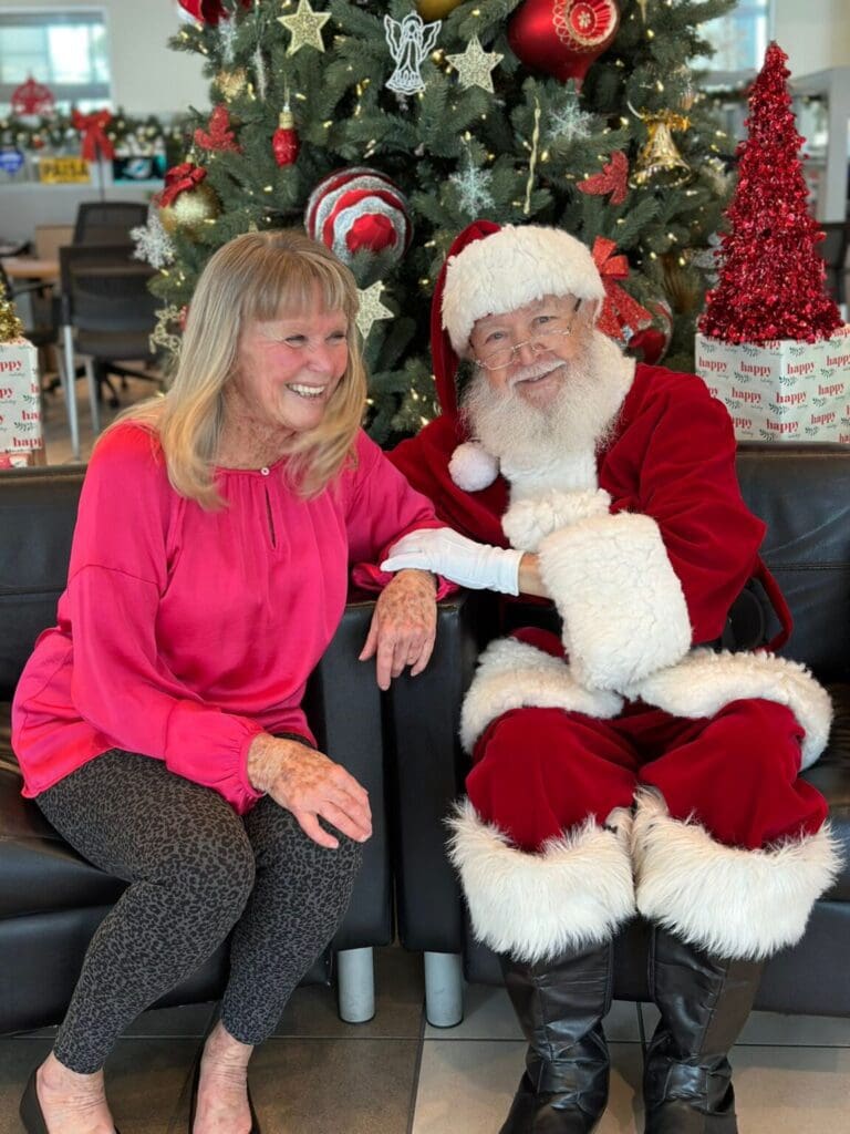 A woman smiles next to Santa Claus in festive attire.
