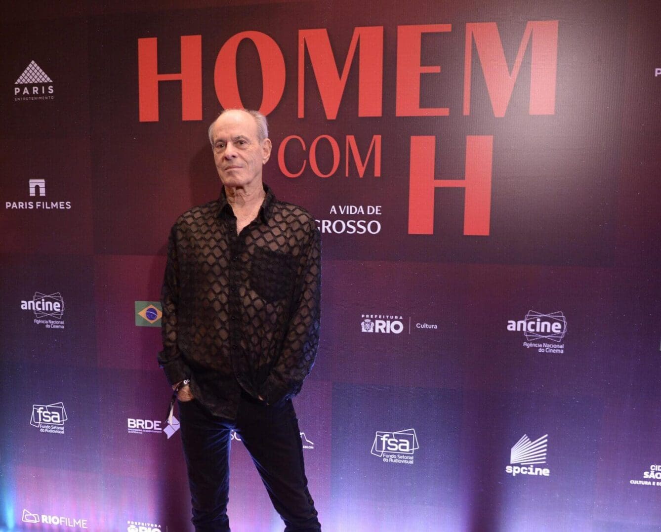 Man posing in front of a Homem Com H event backdrop.
