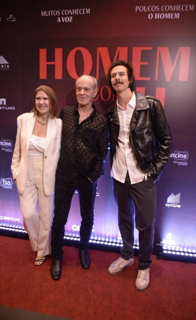 Three people posing on a red carpet at an event.