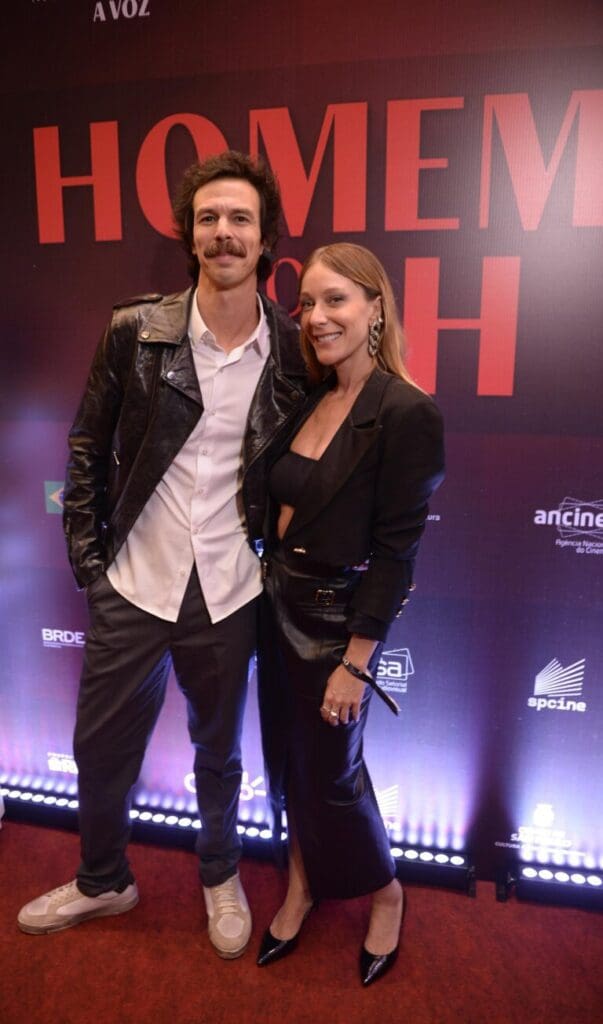 A man and woman posing together at an event with a branded backdrop.