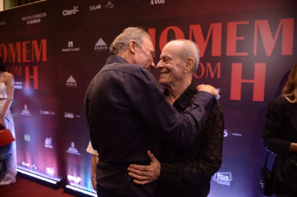 Two men embracing warmly at an event with a backdrop.