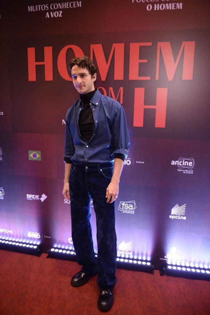 Man posing confidently in casual attire with a lit backdrop.