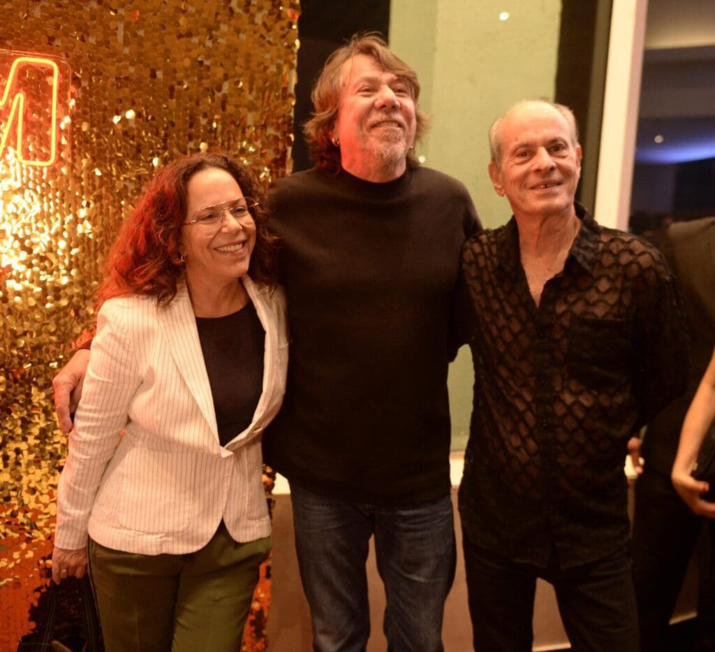 Three people smiling together indoors during a festive gathering.