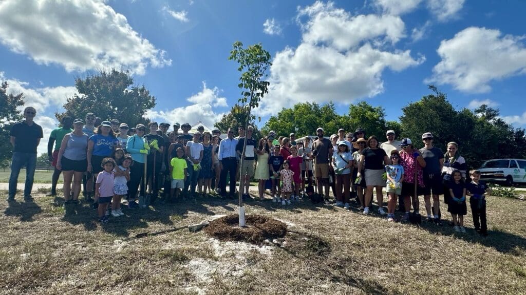 Large group posing outdoors on a sunny day near a fire pit.