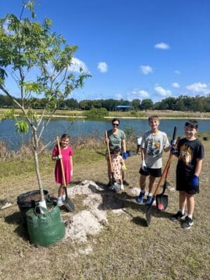 Group of children cleaning a lakeside area with trash bags and tools.