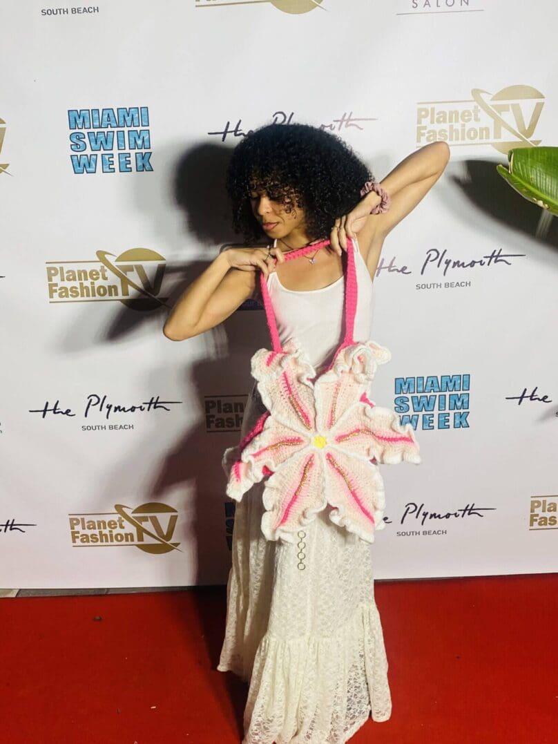 Model in white dress with pink accents posing on red carpet.