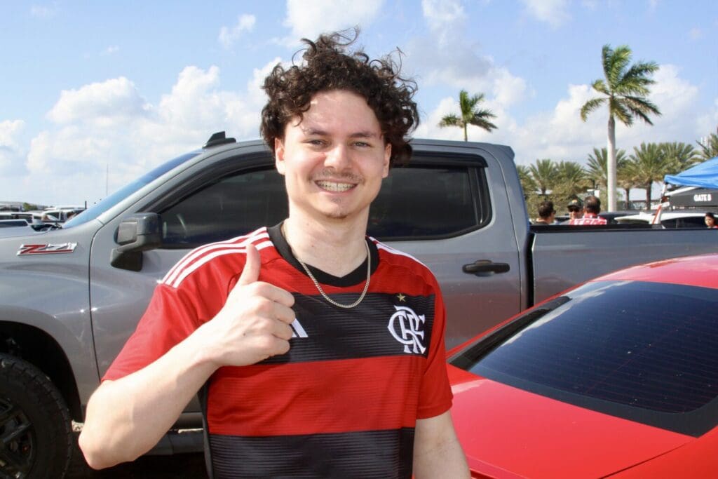 A smiling young man giving a thumbs-up in a red and black striped shirt.