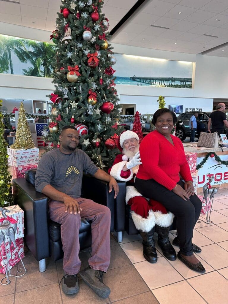 Two adults sitting with Santa Claus beside a decorated Christmas tree.