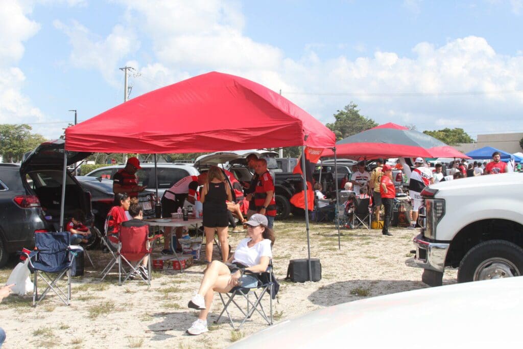 People gathered under red tents at an outdoor event on a sunny day.