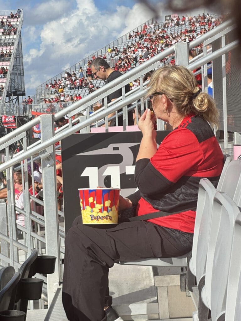 A woman in a red shirt takes photos at a stadium event.