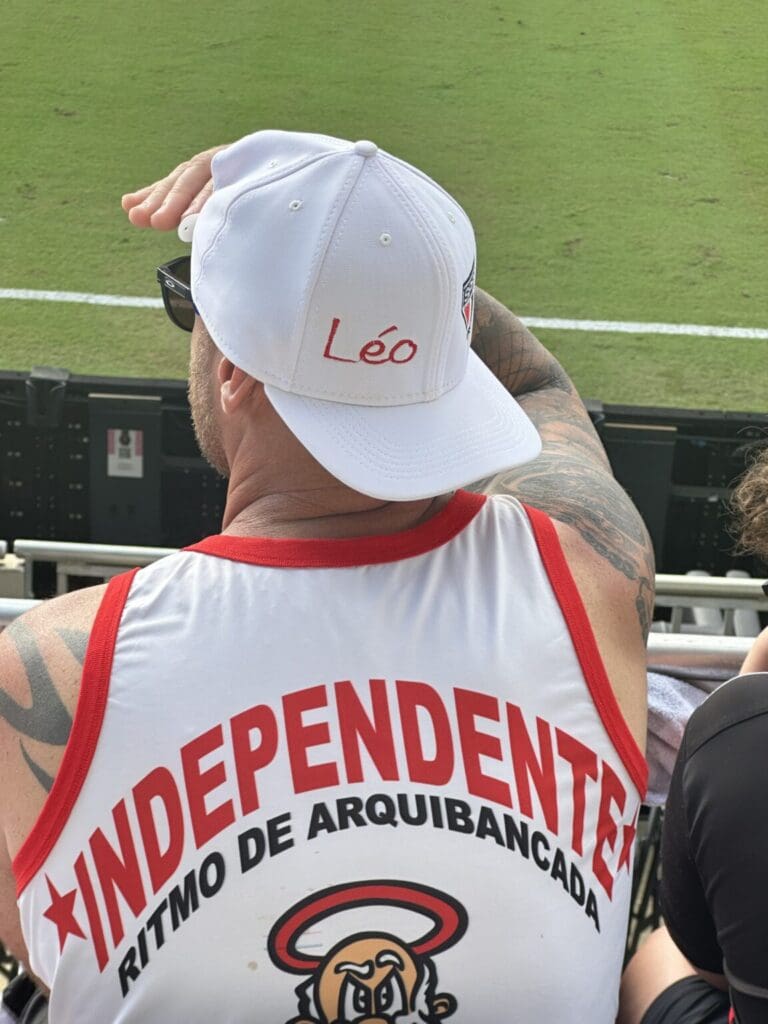 Man wearing a white cap with "Léo" and a red and white shirt at a sports event.
