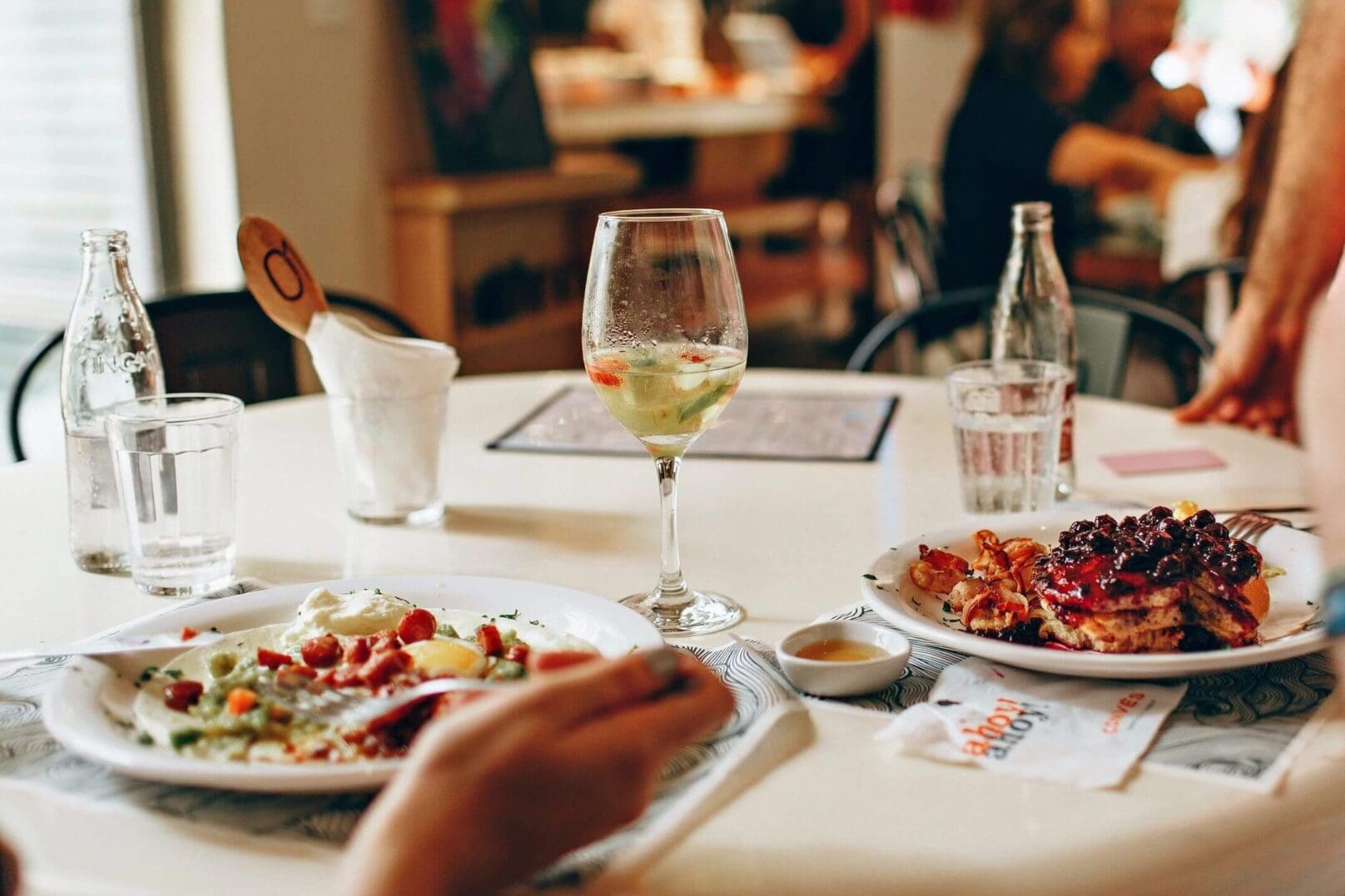 A person dining with wine and a plate of food on a white tablecloth.