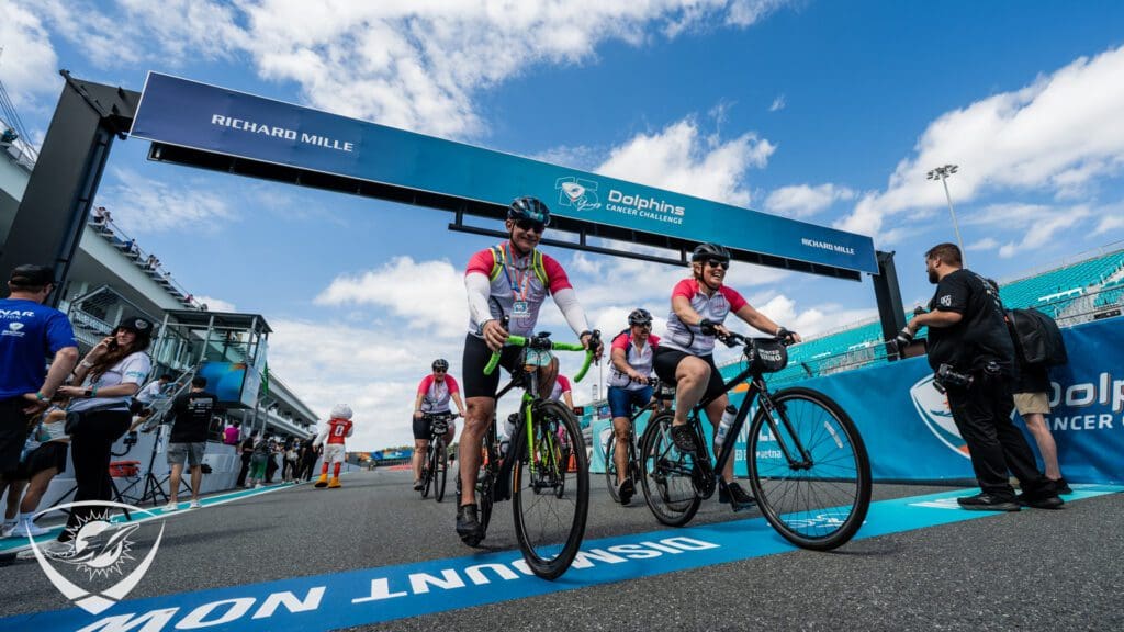Cyclists crossing finish line under blue sky.