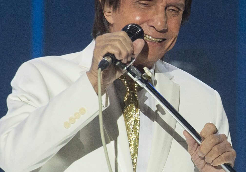 Singer in white suit holding microphone.