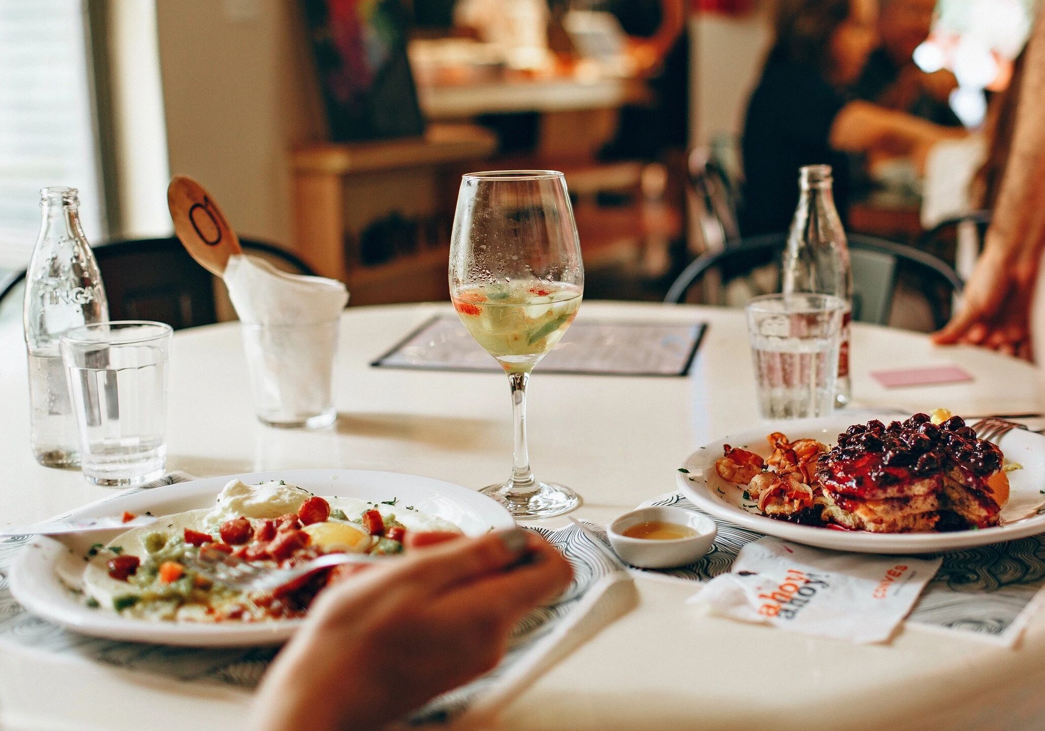 A person dining with wine and a plate of food on a white tablecloth.