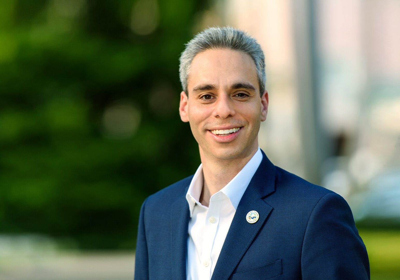 Young man in a blue suit smiling outdoors.